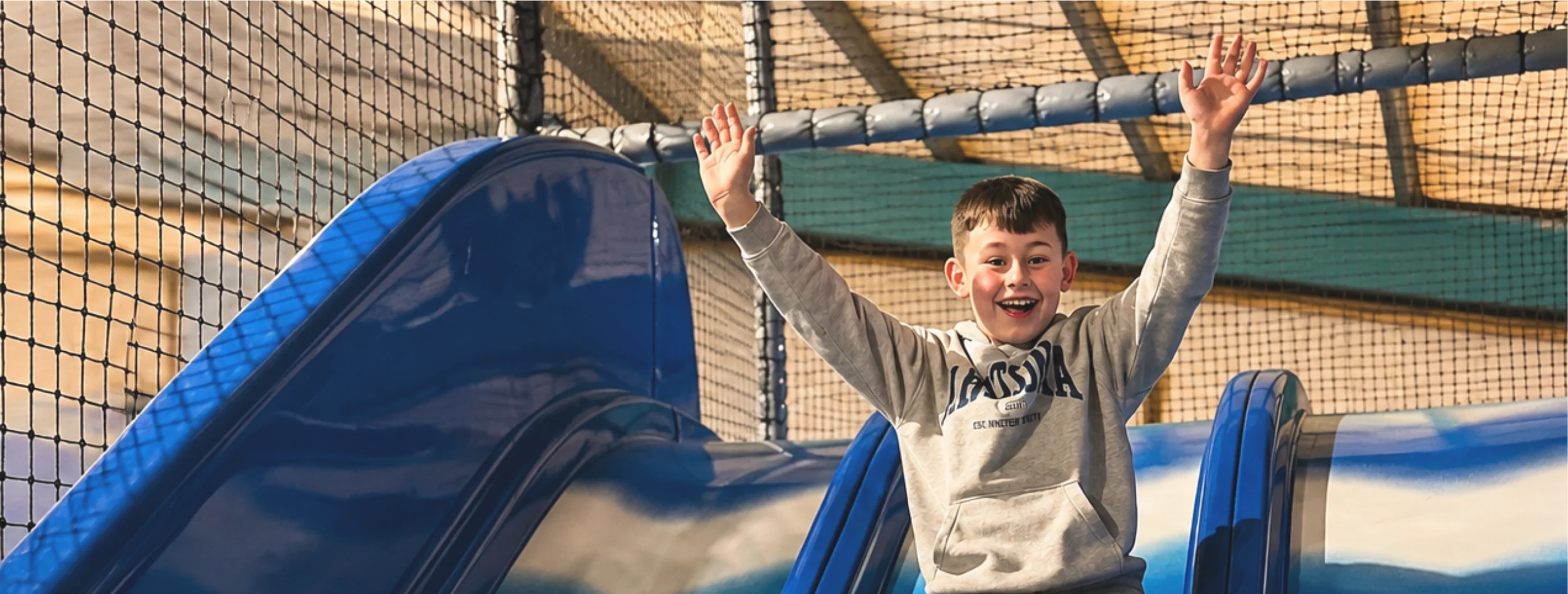 A boy sliding down the soft play slide with his arms in the air